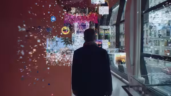 A man stands before a wall of floating digital images beside large windows