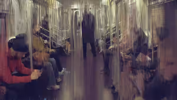 People sit in rows beneath hanging strands in a dim corridor