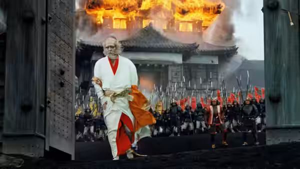 Elderly man in white robes walking from a burning castle gate