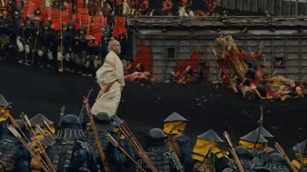Elderly man in white robes standing amid soldiers and fallen bodies