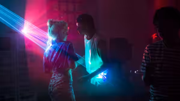 Milla dances with Moses beneath colored lights at a party