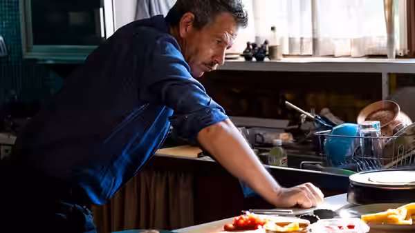 Henry (Ben Mendelsohn) leans over a kitchen counter preparing food