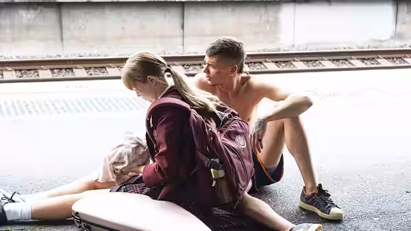 Moses sits beside an injured girl on a railway platform as Milla tends to her
