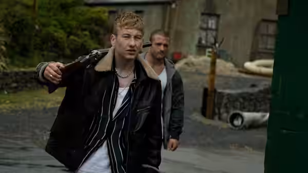 Dympna (Barry Keoghan) walks ahead of Arm (Cosmo Jarvis) through a rural yard
