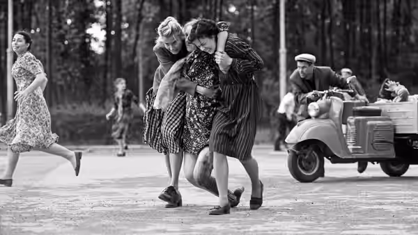 Two women support an injured woman as another runs past a military vehicle