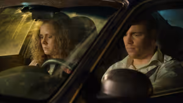 A woman and a man sit silently inside a car