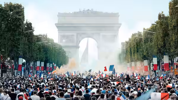 A massive crowd waves French flags and fills the avenue beneath the Arc de Triomphe