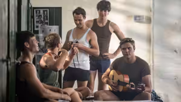 Young soldiers gather in a barracks as one plays guitar