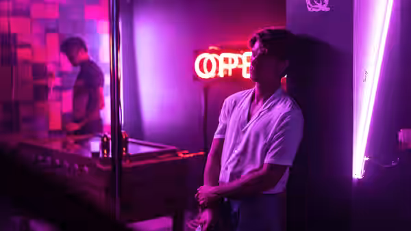 A young man stands beside a pool table in a neon-lit room