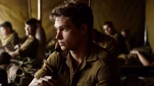 A young soldier sits pensively among other recruits in a barracks