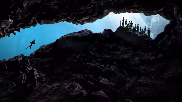 A diver jumps from rocks into blue water while a group watches from a cave ledge