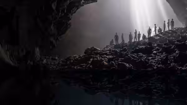 Silhouetted people stand on rocks inside a cave with light beams shining from above