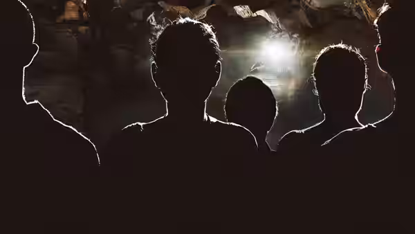 Silhouetted heads of several people gaze out from a dark cave toward bright light