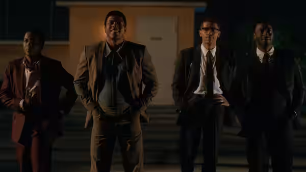 Four men in suits stand together outside a building at night