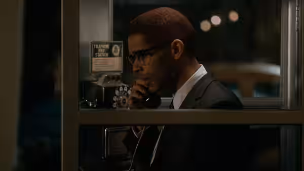 Malcolm X (Kingsley Ben-Adir) speaks on a payphone inside a booth