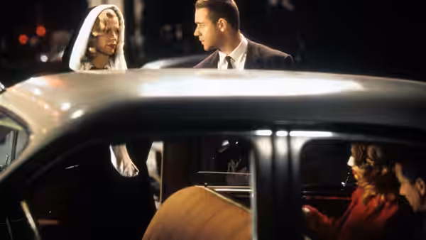 a woman in a headscarf stands beside a vintage car at night talking to a man