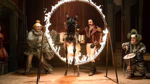 Mangiafuoco stands beside a donkey passing through a ring of fire, with two performers nearby