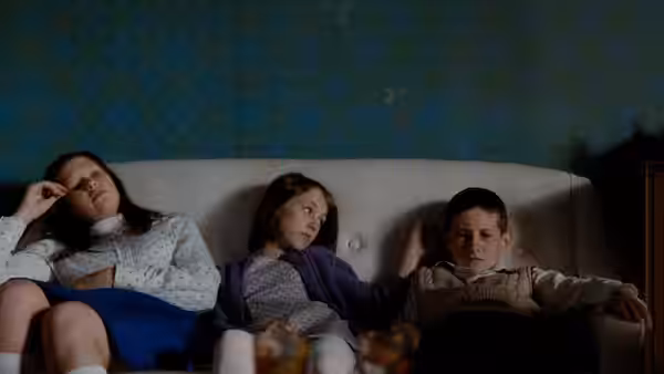 Three children sit together on a white sofa in a living room