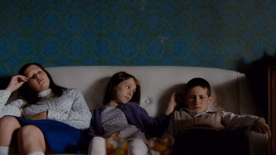Three children sit together on a white sofa in a living room