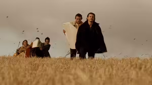 A group of people walk through a field carrying white mattresses