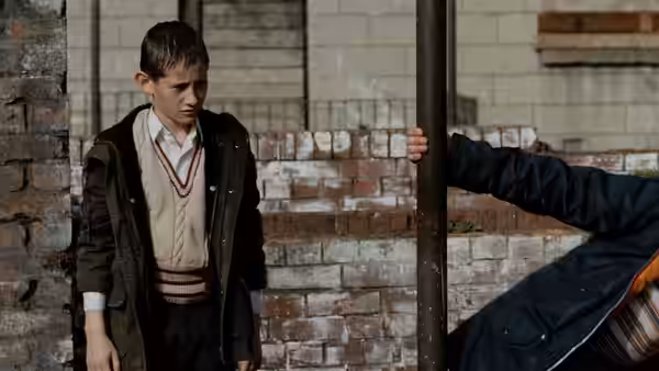 James (William Eadie) stands beside a pole near a brick wall