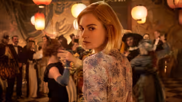 Mrs. de Winter (Lily James) looks back at a crowded party beneath hanging lanterns