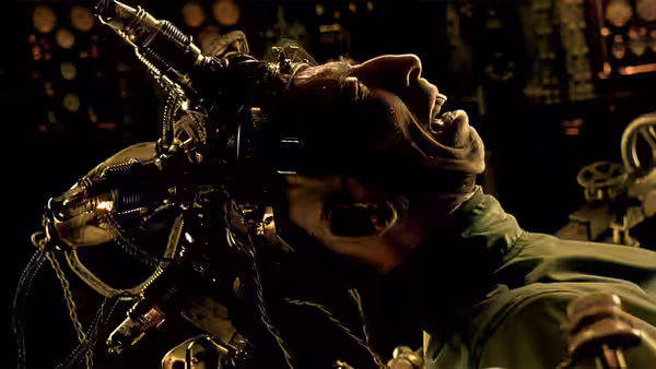 A man with a mechanical headpiece reclines with mouth open amid machinery