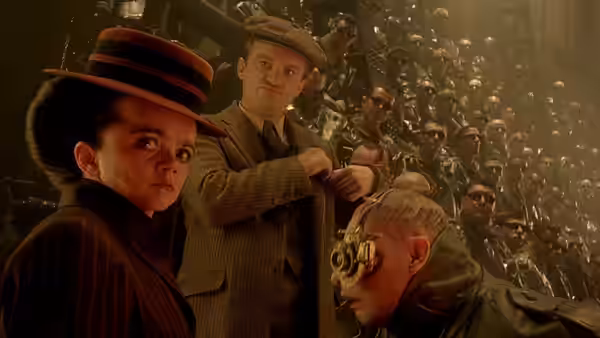 A woman in a brown hat stands before a crowd of men in green uniforms