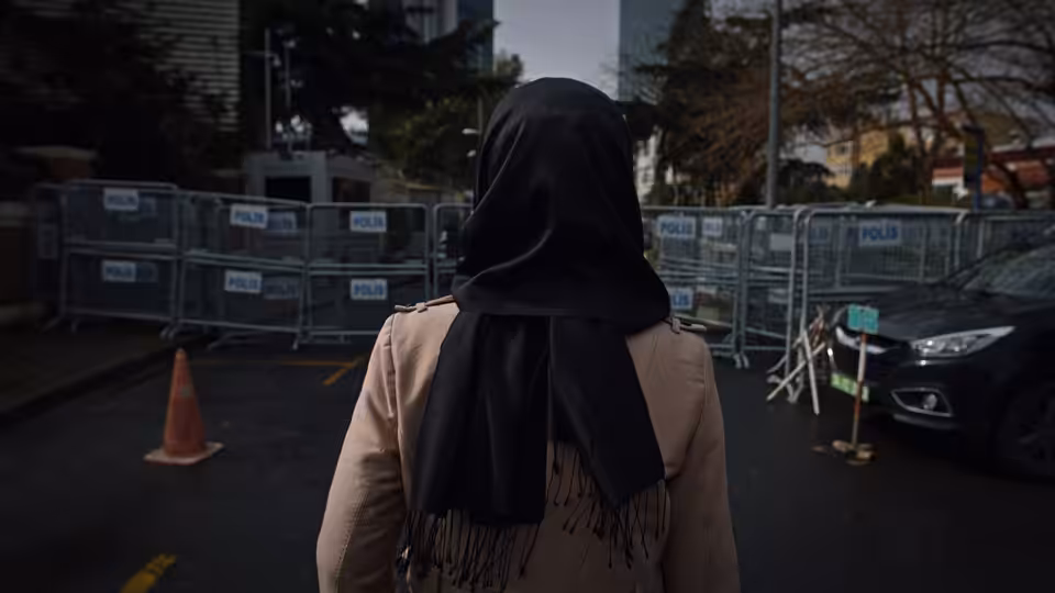 A woman in a black headscarf approaches a police barricade outside a building