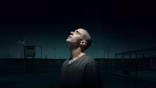 Mohamedou Ould Slahi (Tahar Rahim) stands in a detention yard, looking upward beneath perimeter fencing