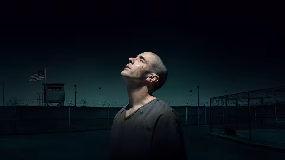 Mohamedou Ould Slahi (Tahar Rahim) stands in a detention yard, looking upward beneath perimeter fencing