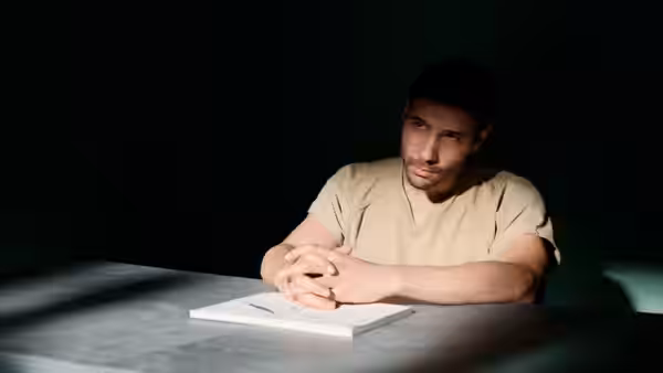 Mohamedou Ould Slahi (Tahar Rahim) sits at an interrogation table with his hands folded