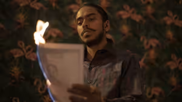 Balram (Adarsh Gourav) reads a document in a room with patterned wallpaper