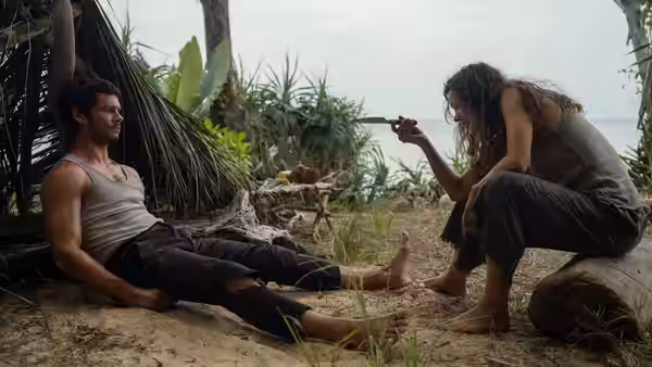 Bradley Preston (Dylan O'Brien) on the sand as Linda Liddle (Rachel McAdams) holds a blade on a tropical beach