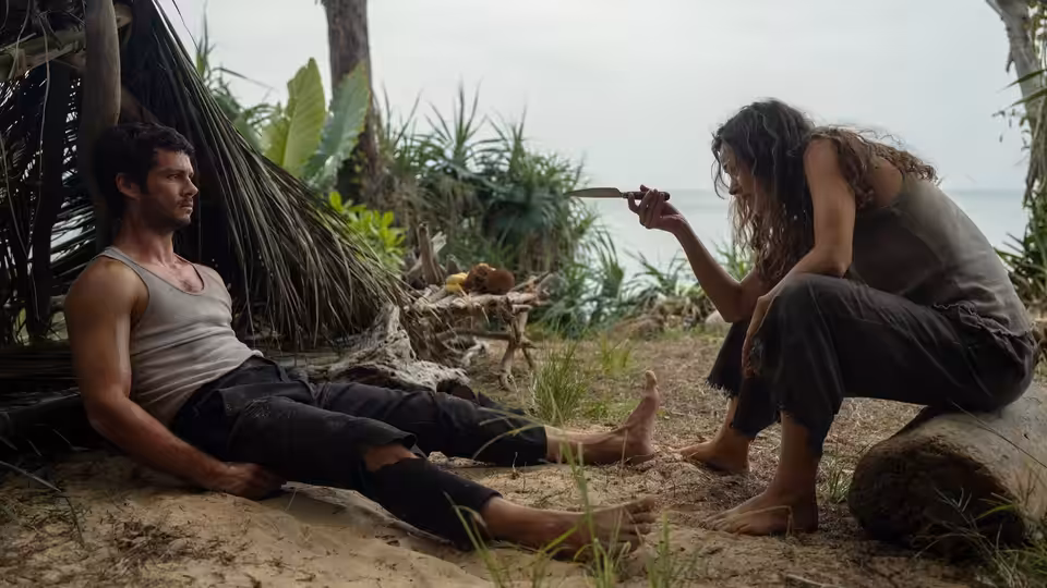 Bradley Preston (Dylan O'Brien) on the sand as Linda Liddle (Rachel McAdams) holds a blade on a tropical beach