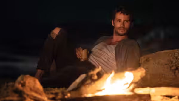 Bradley Preston (Dylan O'Brien) resting beside a campfire on the shore at night