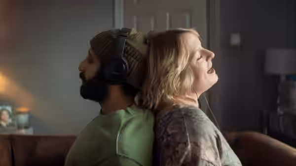 Ali (Adeel Akhtar) and Ava (Claire Rushbrook) sit back to back, sharing headphones indoors