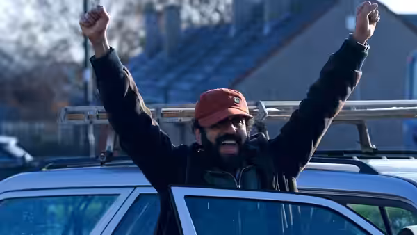 Ali (Adeel Akhtar) beams with both arms raised beside an open car door