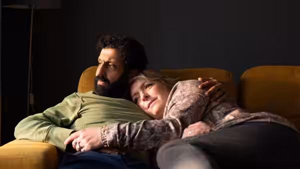 Ali (Adeel Akhtar) sits on a sofa as Ava (Claire Rushbrook) cuddles against him