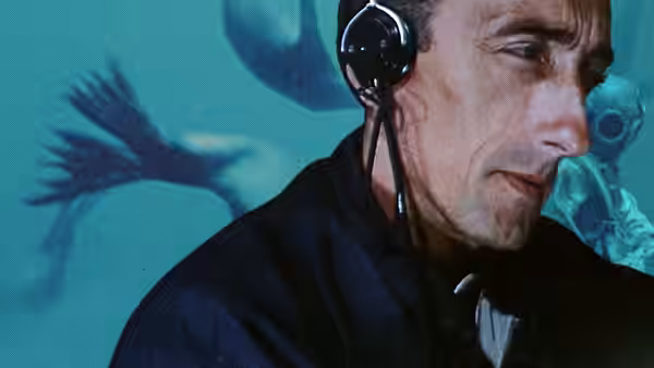 Jacques Cousteau wearing a communications headset as underwater footage plays behind him