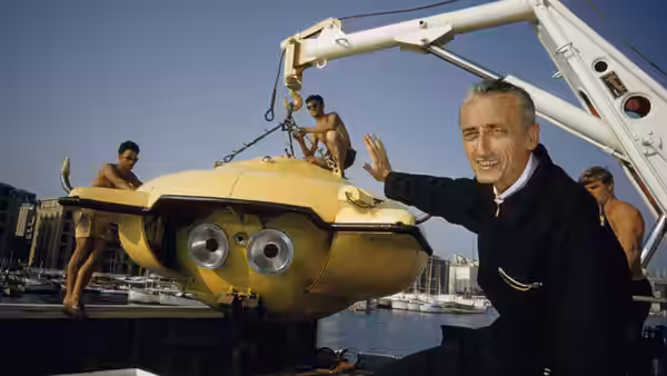 Jacques Cousteau beside a yellow research submersible being lifted aboard a vessel