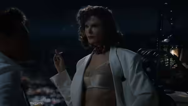 A woman in a white robe holds a cigarette beside a man in a dim room