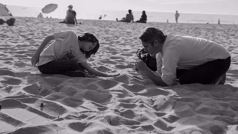 Johnny (Joaquin Phoenix) and Jesse (Woody Norman) kneel in the sand on a beach