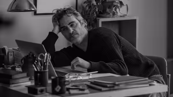 Johnny (Joaquin Phoenix) leans on his hand beside a laptop at his desk