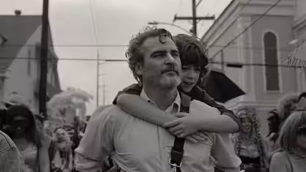 Johnny (Joaquin Phoenix) carries Jesse (Woody Norman) through a crowded street festival