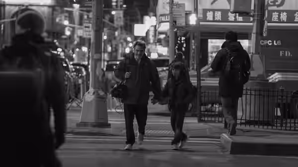 Johnny (Joaquin Phoenix) and Jesse (Woody Norman) walk hand in hand along a busy city street