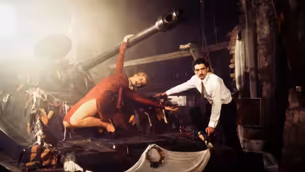 a woman in red reaching across a large cannon toward a man in a shirt