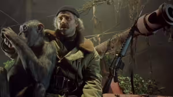 a man in a beret with a monkey on his shoulder beside a large gun