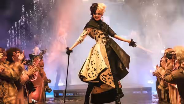 Cruella (Emma Stone) poses with a cane as a crowd cheers around her