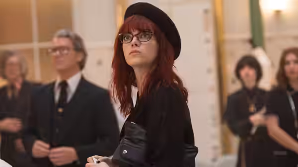 Estella (Emma Stone), wearing glasses and a beret, looks upward at a gathering